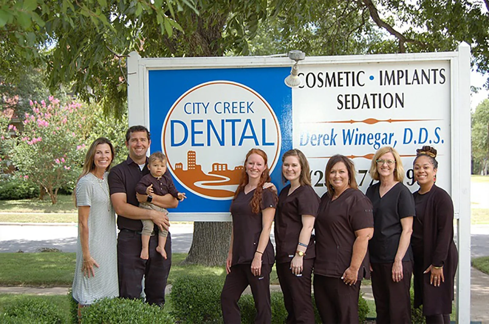 Picture of the staff at city creek dental in front of the sign outside the office.